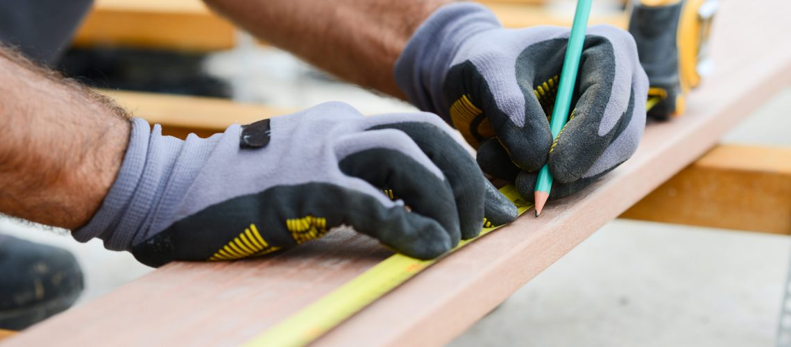close up detail of manual worker hands working with a measuring tape and pencil in wood plank